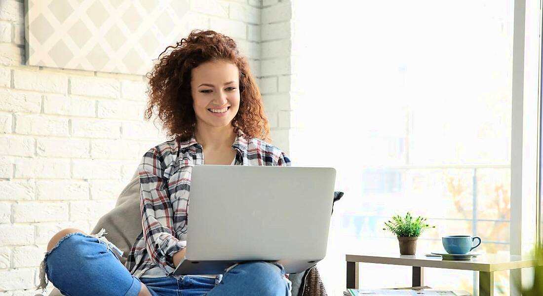 A woman sitting cross-legged while working on her laptop in a bright room.