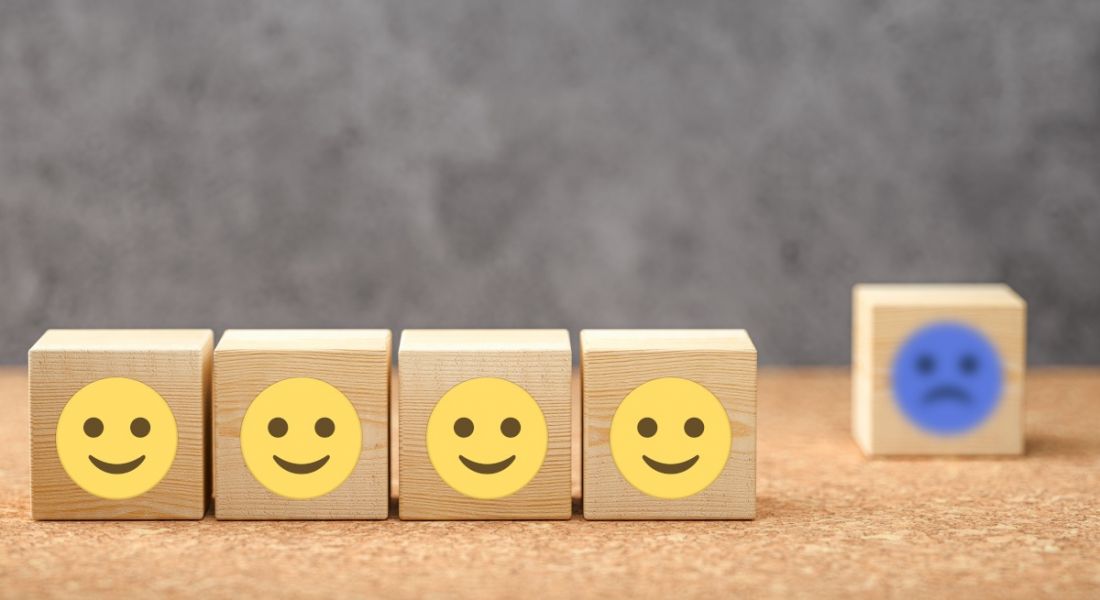 A row of four wooden cubes with yellow smiley faces. In the background there is a single wooden cube with a blue sad face, symbolising proximity bias.