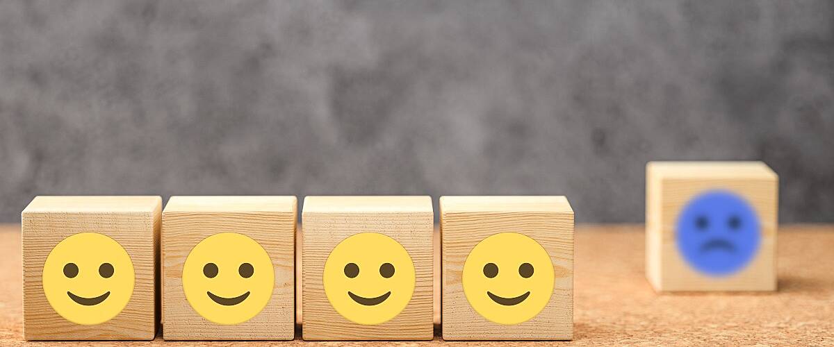 A row of four wooden cubes with yellow smiley faces. In the background there is a single wooden cube with a blue sad face, symbolising proximity bias.
