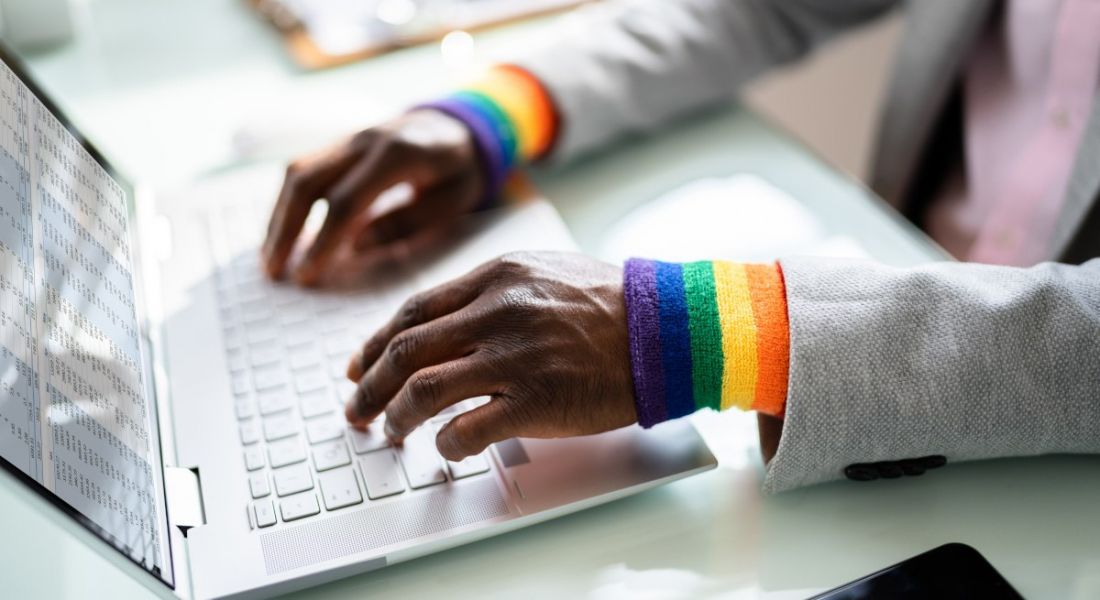 A close-up of a person's hands typing at a keyboard wearing rainbow-coloured wristbands, symbolising LGBTQ+ in the workplace.