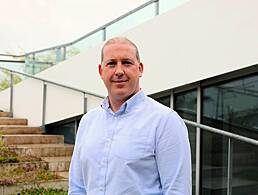 A man sits in a room with a whiteboard and a wall behind him. He is Mark Stewart, a software architect at Yahoo.