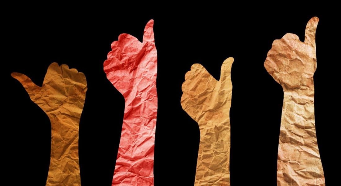 Different colour hands made out of paper raising the thumbs up on a dark background representing a DEI strategy.