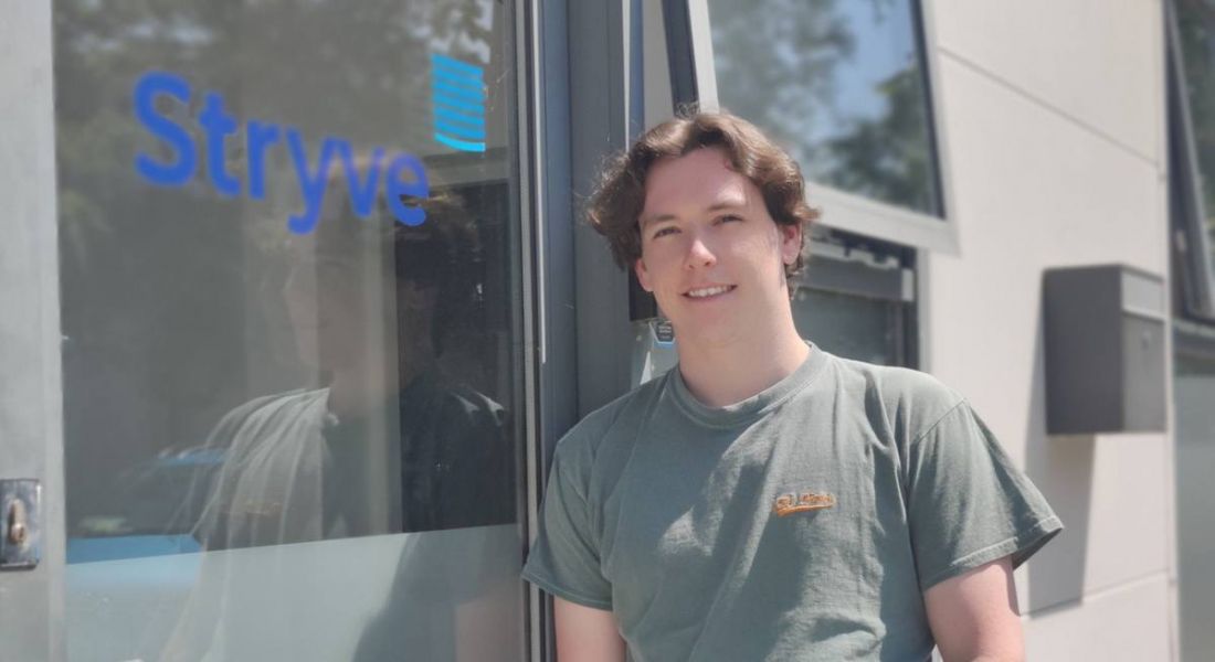 Andrew Cushen leaning against a window or door of a building with the word Stryve on it in blue.