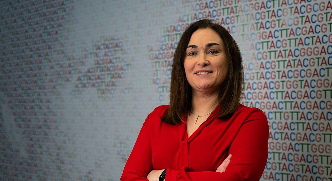 A woman wearing a red blouse smiles at the camera with her arms folded. She is Karen Breen, a risk and business performance director at Amgen.