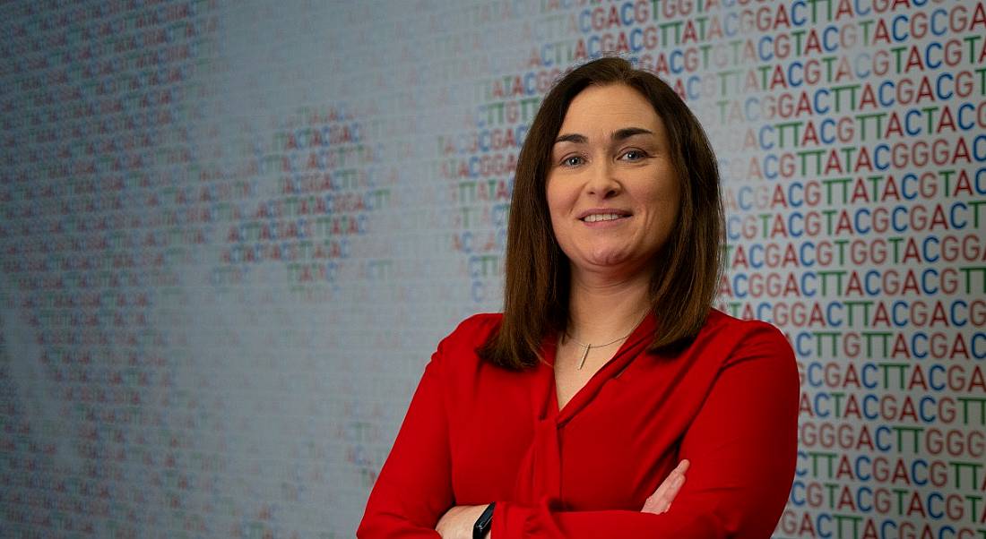 A woman wearing a red blouse smiles at the camera with her arms folded. She is Karen Breen, a risk and business performance director at Amgen.