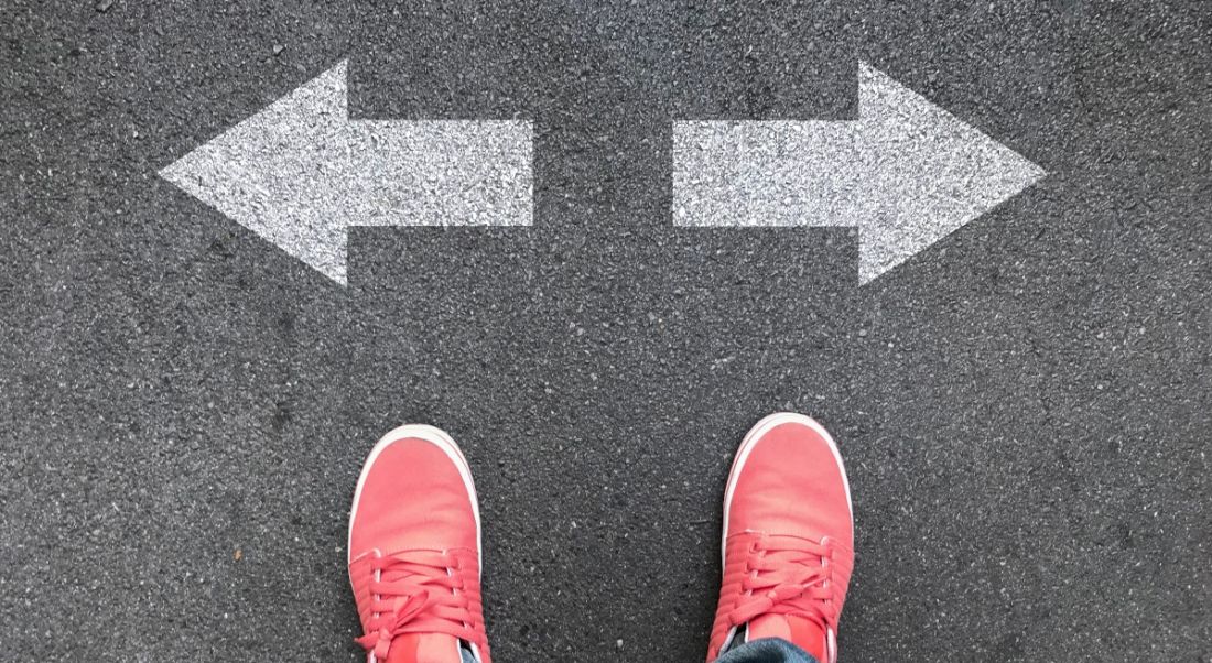 A pair of feet in red shoes in front of two opposing arrows.