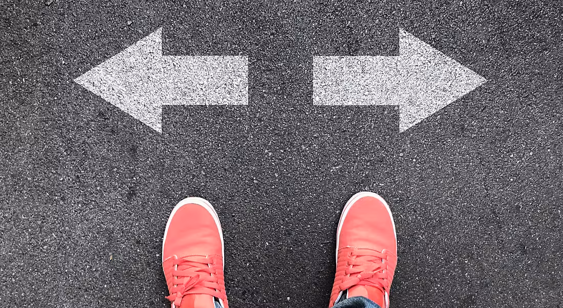 A pair of feet in red shoes in front of two opposing arrows.
