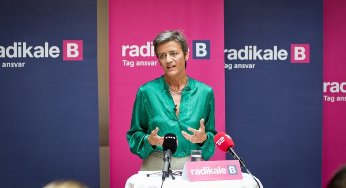 Margrethe Vestager standing at a podium speaking to the press.