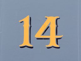 A sign with the number 18 on a brown brick wall next to the front door of a house.