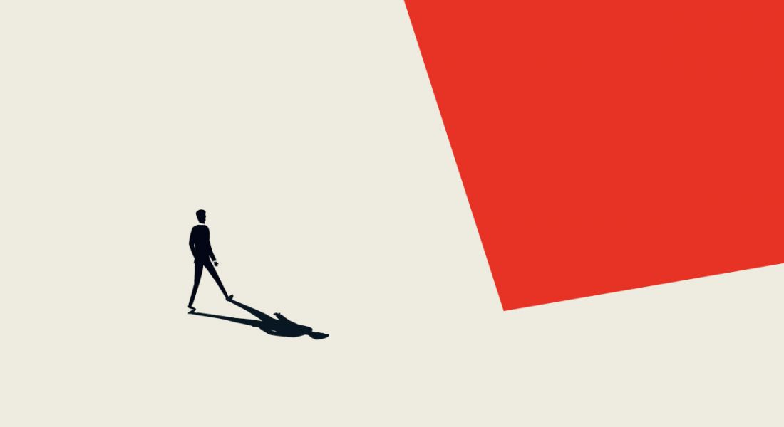 A silhouette of an individual with its shadow in view on a beige and red abstract-shaped background.