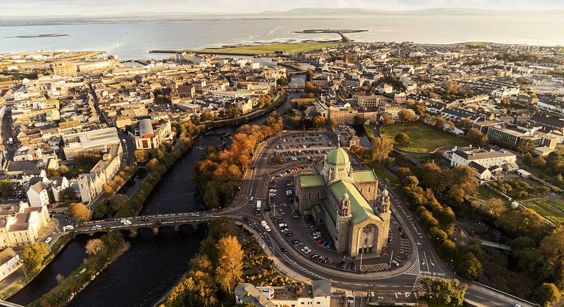 An aerial view of Galway cathedral at sunset with the city visible around it and the sea in the background.