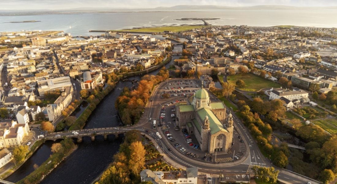 An aerial view of Galway cathedral at sunset with the city visible around it and the sea in the background.