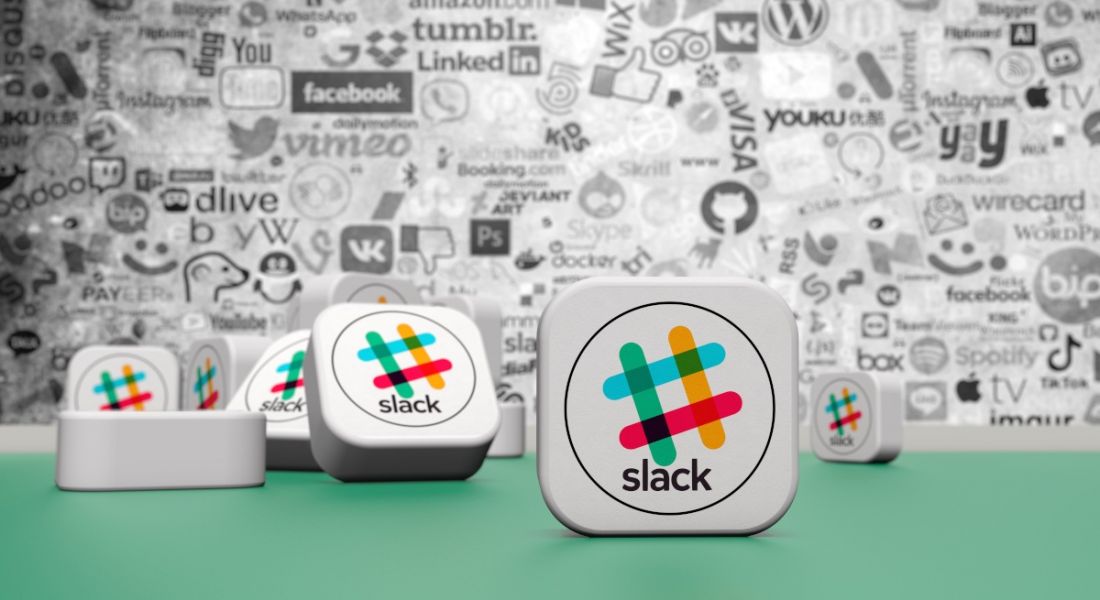 Slack logos on boxes that are scattered on a green surface with a wall full of logos and writing in black and white.