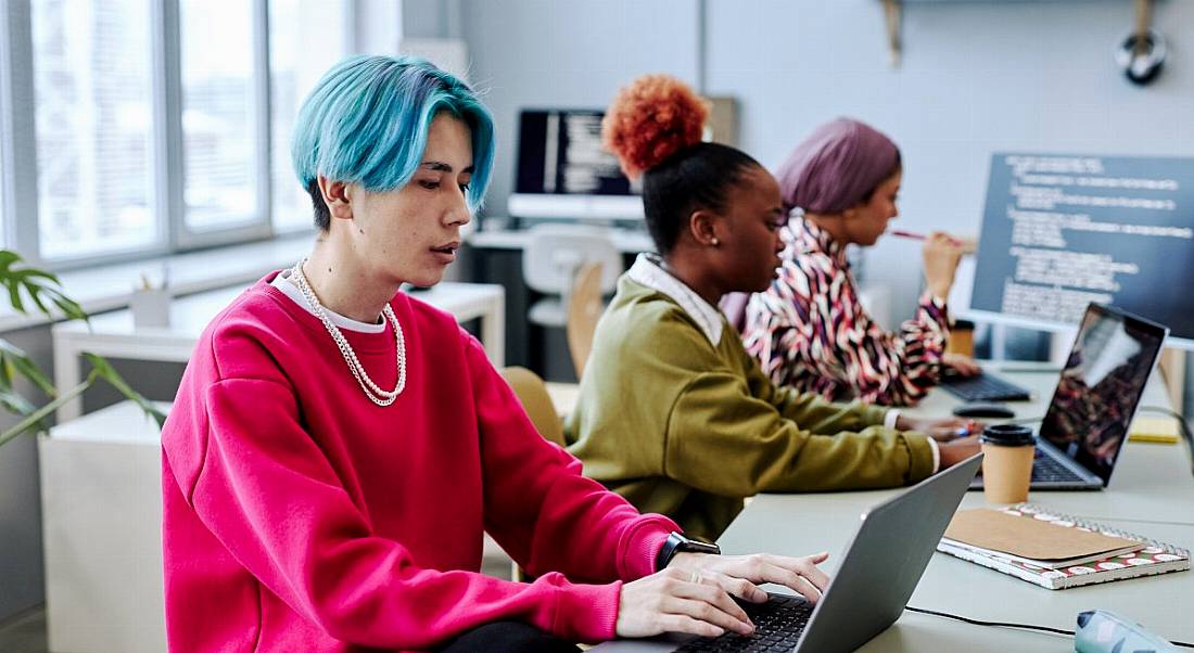 Three Gen Z tech workers working on computers in an office environment.