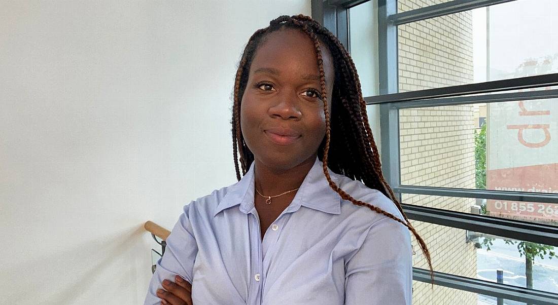 A woman wearing a light blue shirt smiles with her arms crossed in an office setting. She is Blessing Folayan, a radiographer and technology consulting analyst at Deloitte.