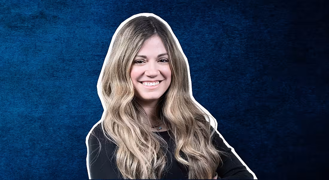 A headshot of a woman with long hair smiling at the camera against a blue background. She is Christina Gialleli.