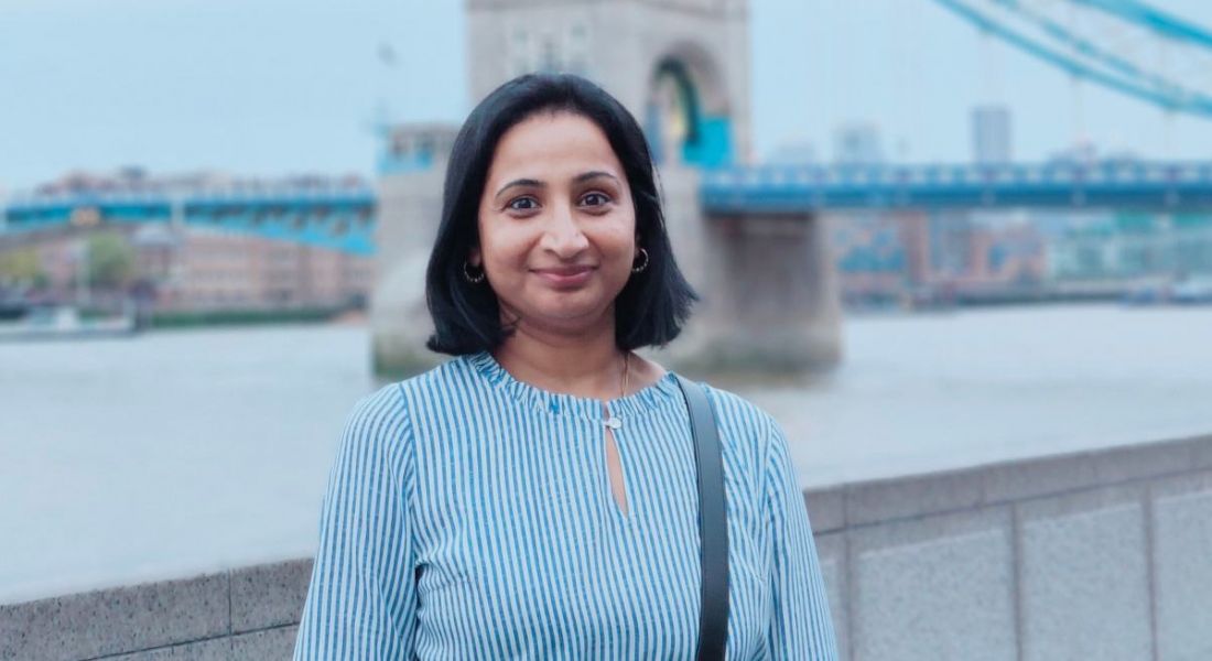 A woman smiles while standing with London's Tower Bridge sits behind her. She is Priyanka Lingegowda, a principal software engineer at Liberty IT.