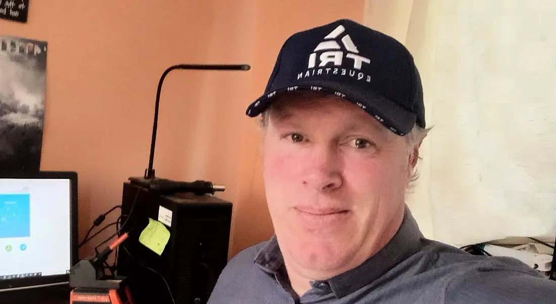 A man wearing a baseball cap smiles at the camera in a home office setting. There is a brown wall behind him as well as a computer. He is Shaun Haren, a software development intern at Fidelity Investments.