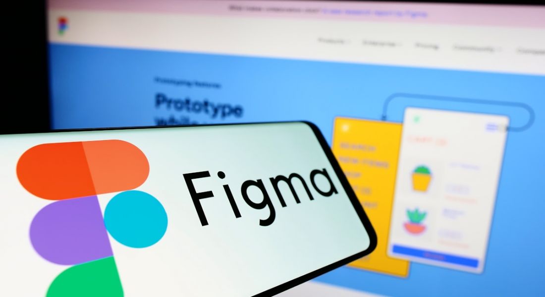A phone with the Figma logo on it held up in front of a laptop with the Figma website.