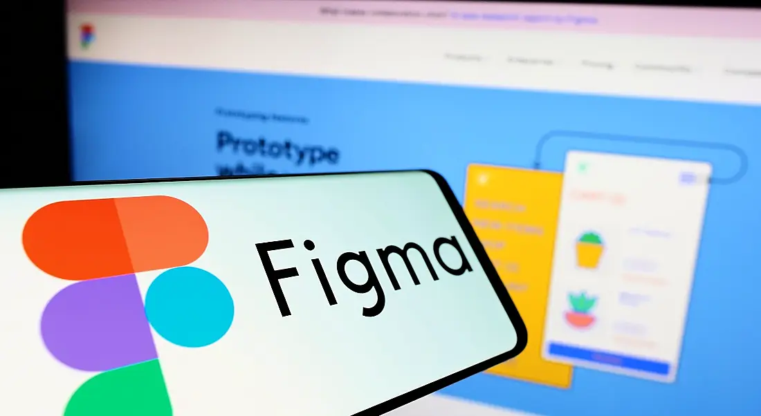 A phone with the Figma logo on it held up in front of a laptop with the Figma website.