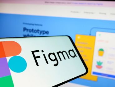 A phone with the Figma logo on it held up in front of a laptop with the Figma website.