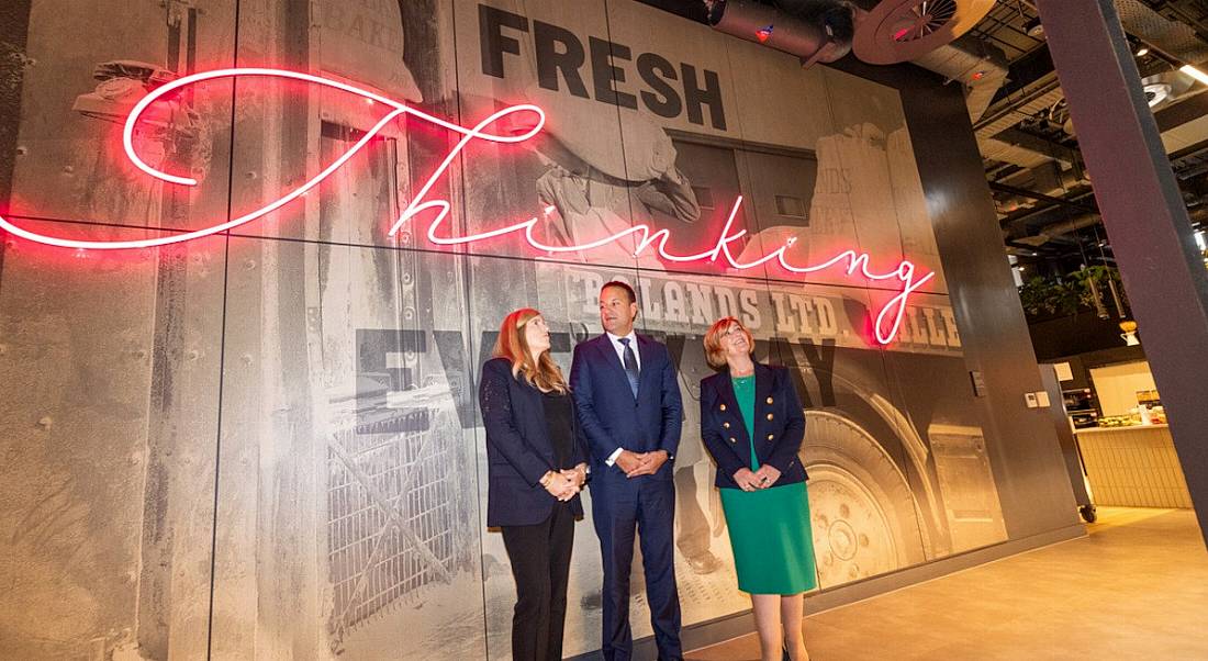 Three people standing against a trendy, fake wood panelled banner for Google's Boland Mills development.