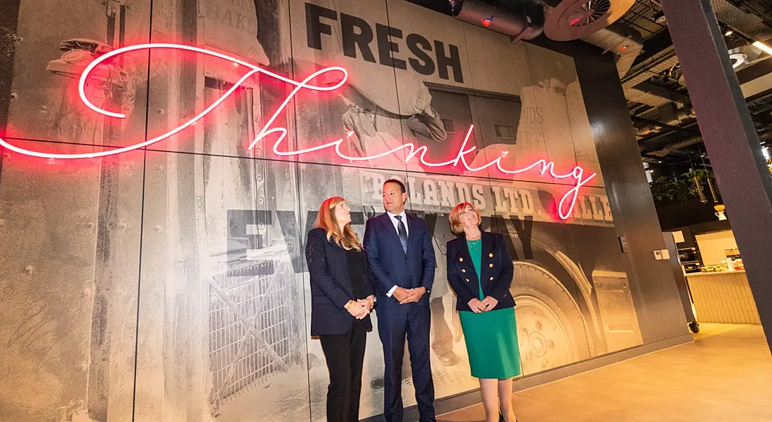 Three people standing against a trendy, fake wood panelled banner for Google's Boland Mills development.