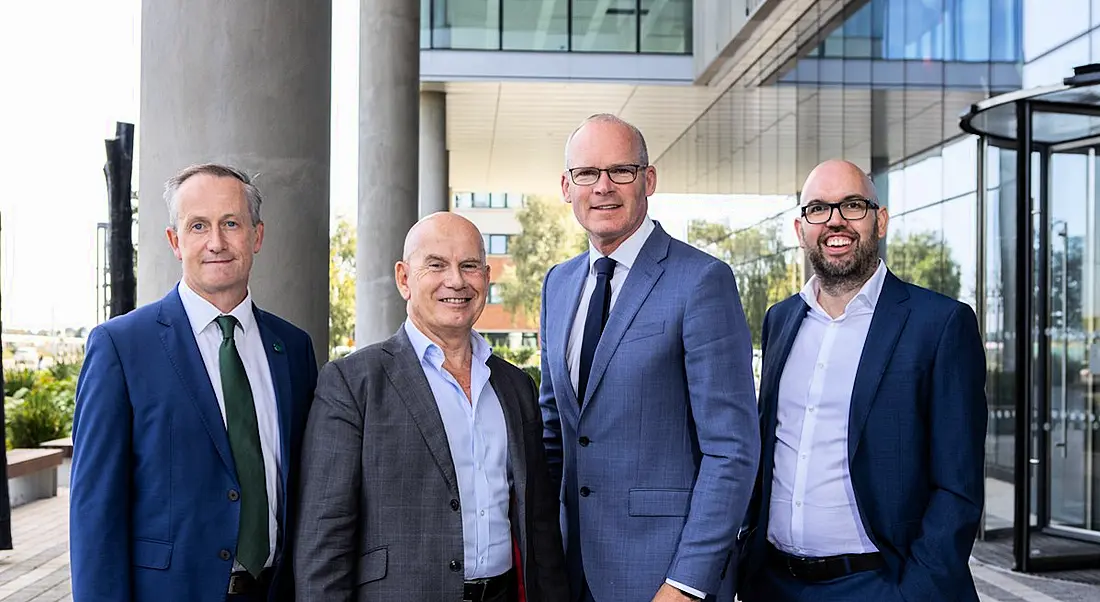 Four men stand in a line outside a modern building on a sunny day smiling at the camera. It is the new Integrity360 building.