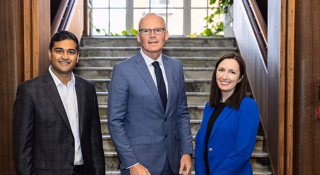 Three people standing in a line together in front of some stairs at the announcement of Rippling moving into Ireland.