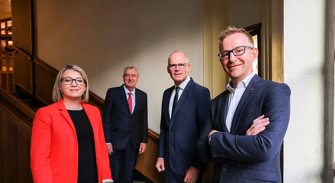 Three men and a woman standing in a room in front of stairs.