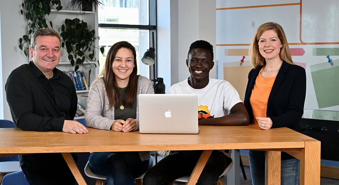 Four people from Liberty IT sitting at a desk with a laptop in an office.