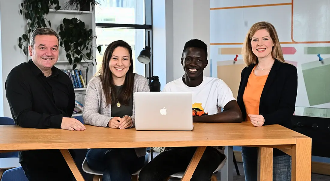 Four people from Liberty IT sitting at a desk with a laptop in an office.