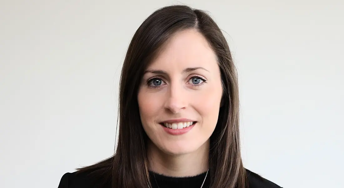 A woman smiles at the camera wearing a dark blazer with a white background behind her. She is Nicola Magill, director of process development at Amgen.