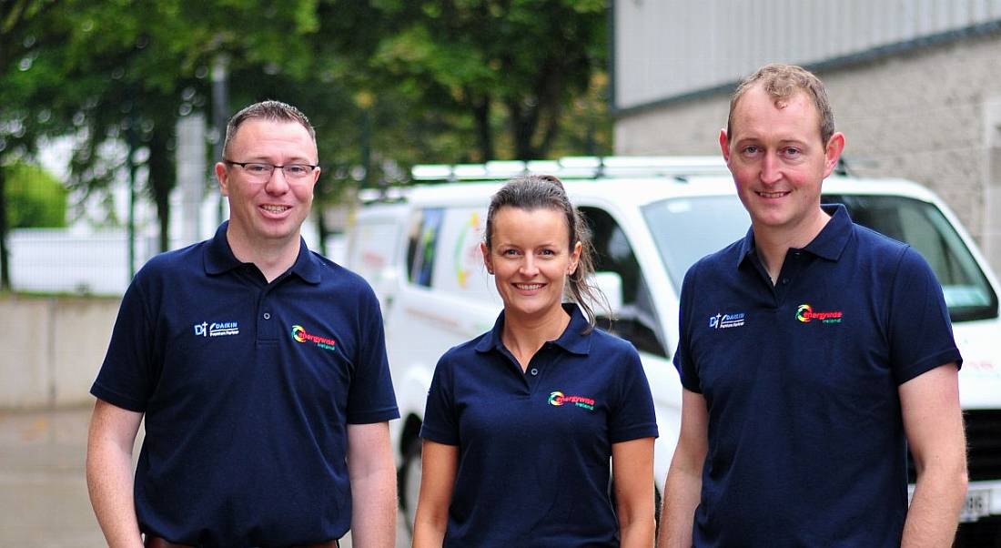 Two men stand on either side of a woman as they pose for a photo wearing t-shirts with the Energywise Ireland logo on them.