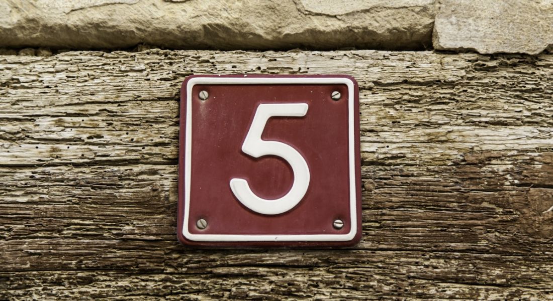 The number five on a brown sign nailed into a plank of wood.