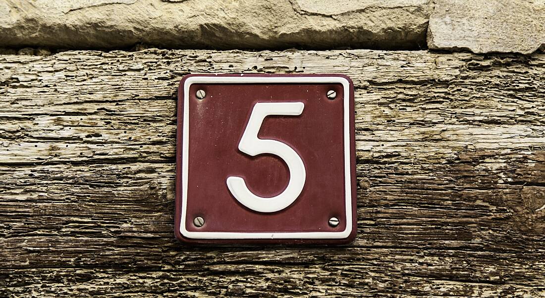 The number five on a brown sign nailed into a plank of wood.