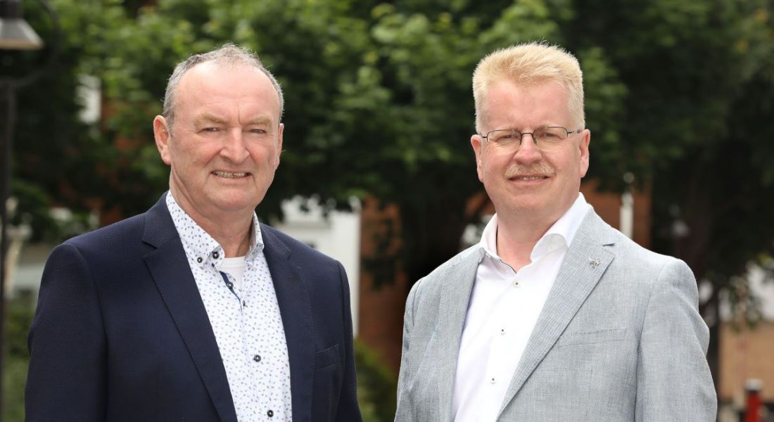 Two men who work at Tekenable standing outside in front of green trees.