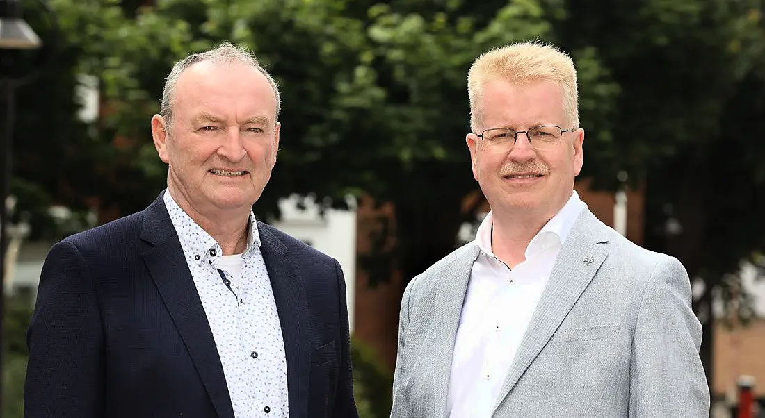 Two men who work at Tekenable standing outside in front of green trees.