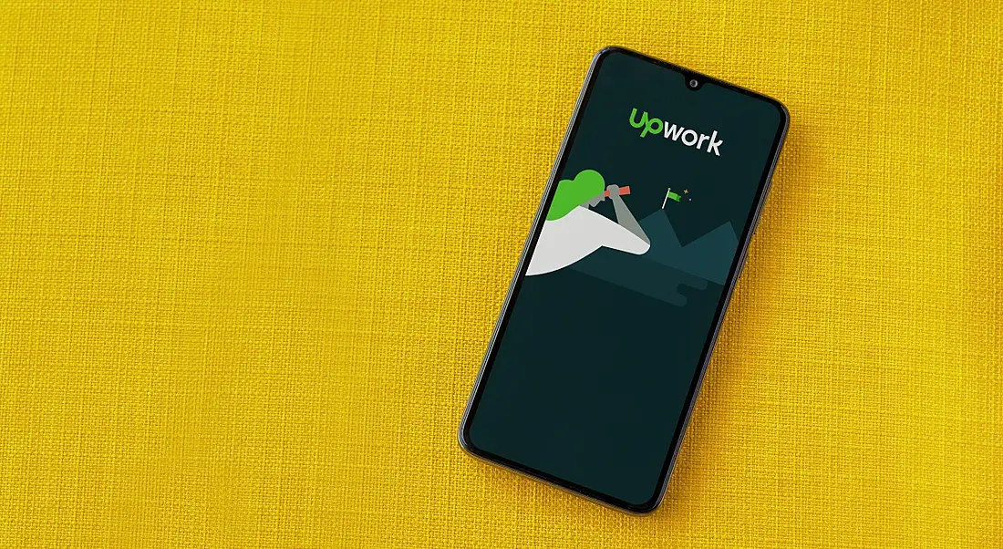 Phone showing Upwork logo and branding on it. The phone is on a yellow background.