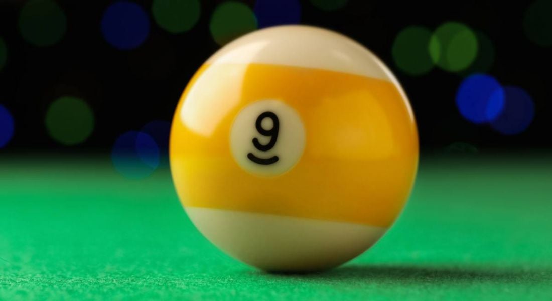 A yellow and white billiard ball with the number nine on it lying on a pool table.