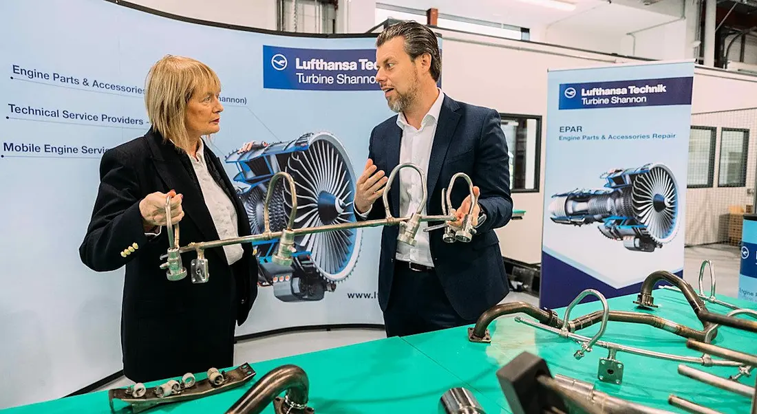 A woman and a man standing at a table with aircraft pieces laid out on a green tablecloth.