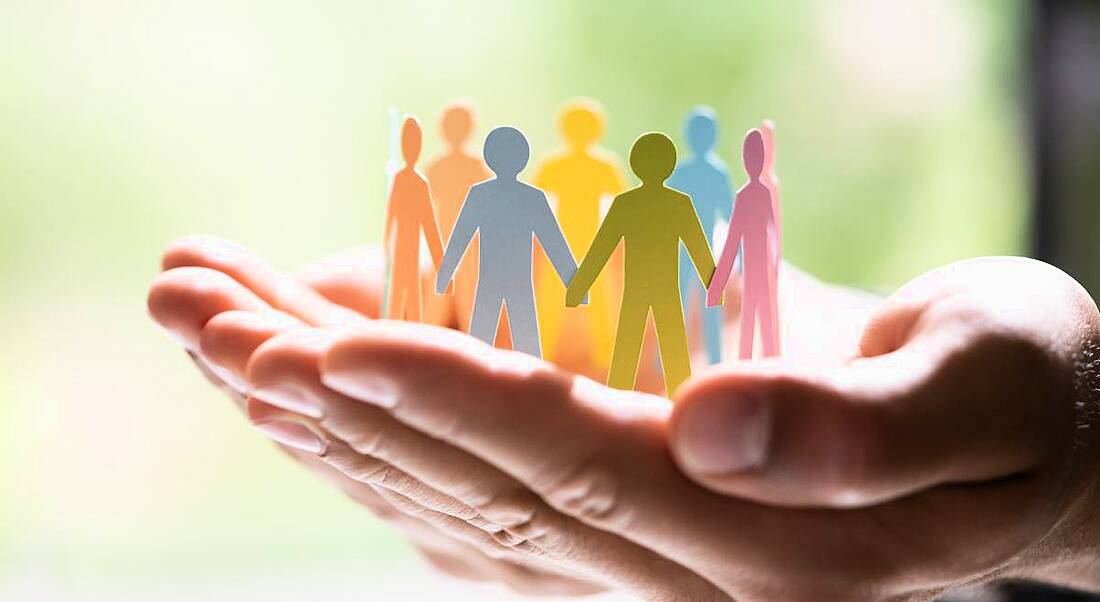 Hands cupped and holding upstanding paper cut-outs of people in different colours, to symbolise diversity.