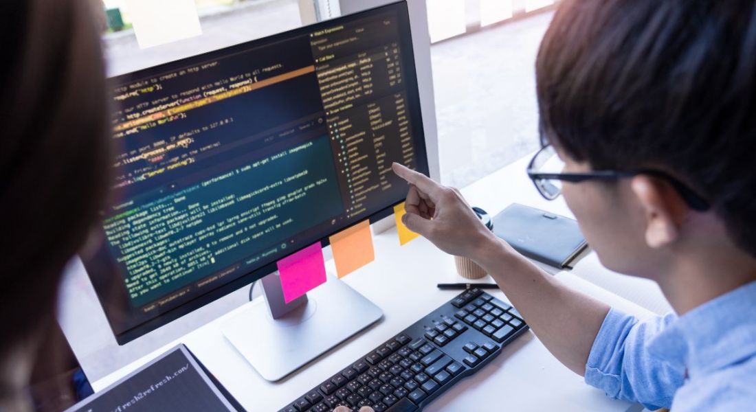 A man sitting at a desk pointing at a screen with a lot of code on it.