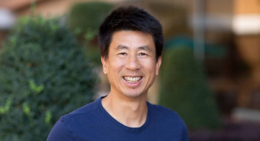 A man wearing a dark blue t-shirt smiles at the camera. Behind him is some shrubbery. He is Sam Liang, CEO of Otter.ai.