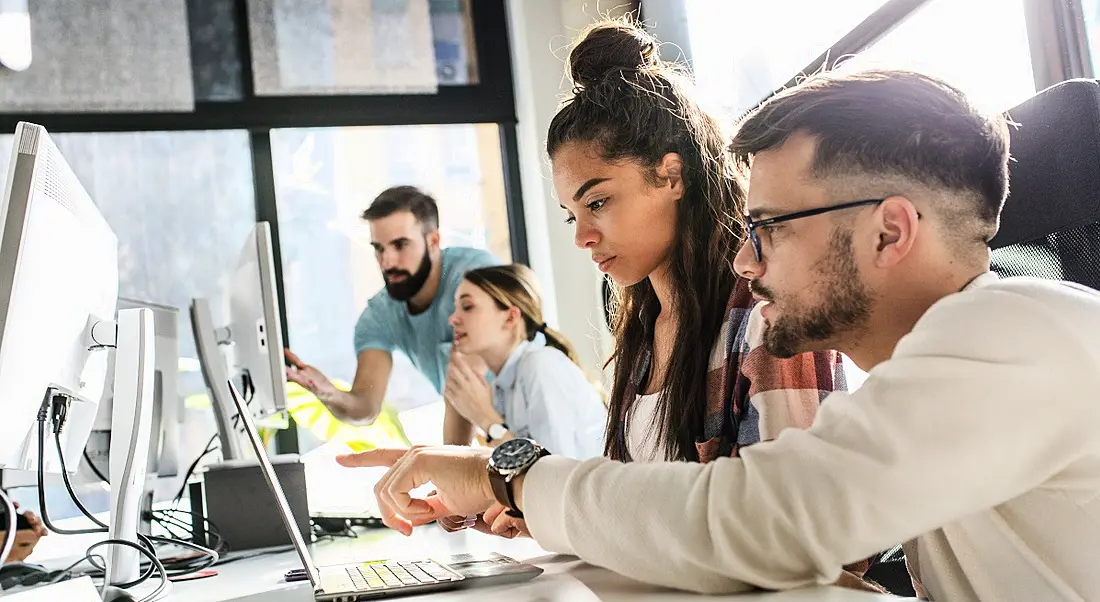 Two young employees being shown how to do things on a computer screen by more experienced employees.