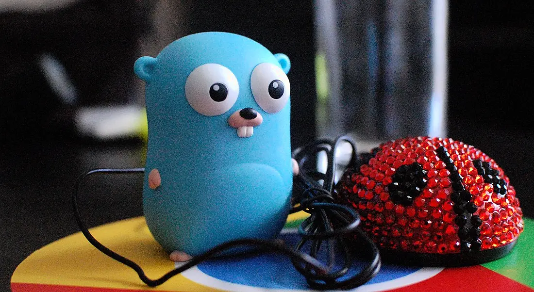 The Golang gopher mascot figurine with a ladybird rhinestone decorated computer mouse sitting on a surface that is designed like the Google Chrome browser logo.