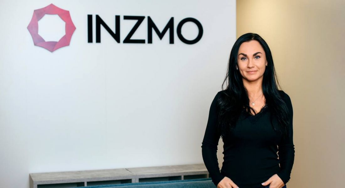 Meeri Savolainen stands in front of a wall with the INZMO logo on it.