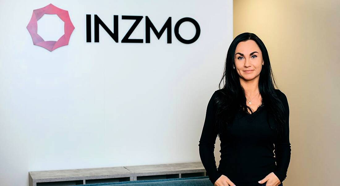 Meeri Savolainen stands in front of a wall with the INZMO logo on it.