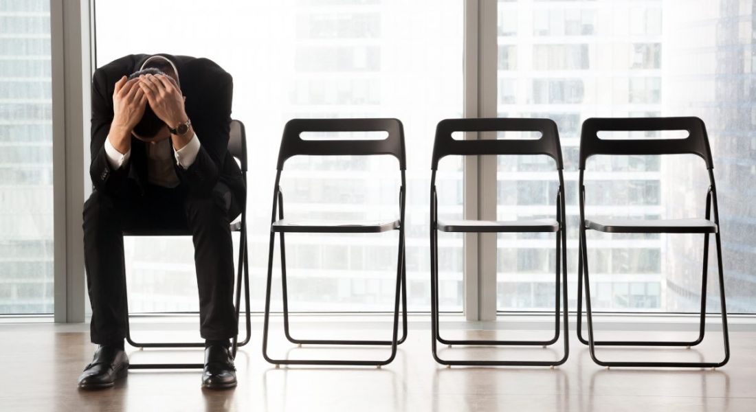 Business person with his head in his hands sitting in a row of empty chairs.