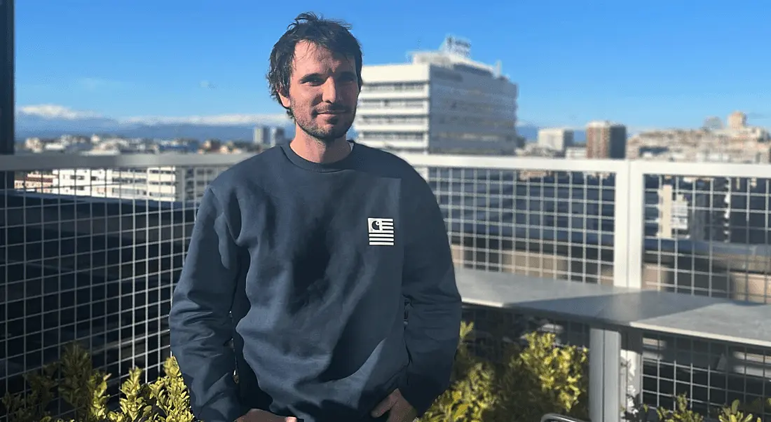 A man stands on a balcony overlooking city buildings in the background while he faces the camera. He is Alessandro Broggio, a people data analyst at Personio.